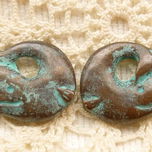 May include: Two antique bronze-coloured dolphin charms with a turquoise patina. The dolphins are curled into a circle with a hole in the centre for threading.