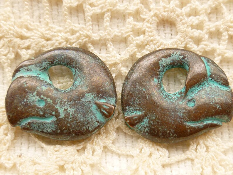 May include: Two antique bronze-coloured dolphin charms with a turquoise patina. The dolphins are curled into a circle with a hole in the centre for threading.