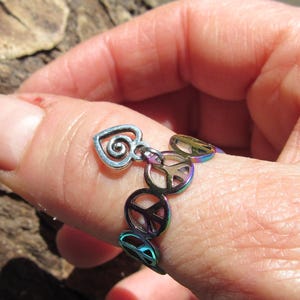 May include: A silver ring with a peace sign charm and a heart charm. The ring is iridescent and has a rainbow effect.