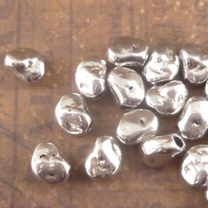 May include: A group of silver-colored metal beads, each with a unique irregular shape and a small hole for stringing.