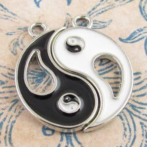 May include: A Yin and Yang charm pendant with a black and white enamel design. The pendant is split into two halves, each with a loop for attaching to a necklace or bracelet. The charm has a silver-coloured border.