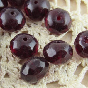 May include: A collection of dark red faceted glass beads. The beads are round and have a hole in the center for stringing.