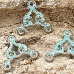 May include: Three ornate metal corner brackets in a teal blue color with a distressed finish. The brackets are triangular in shape with a decorative scroll design.