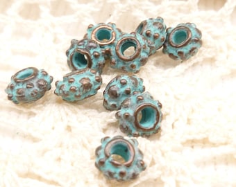 May include: A collection of turquoise and bronze-colored metal beads. Each bead has a textured surface with small, raised bumps and a central hole. The beads have a weathered, antique appearance, suitable for jewelry making or craft projects.