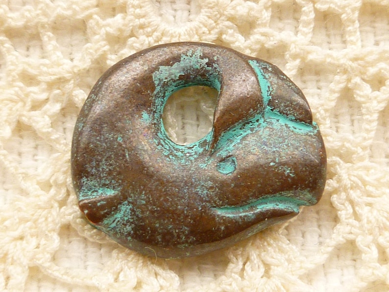 May include: A small, round, bronze pendant with a hole in the centre. The pendant has a green patina and is shaped like a fish.
