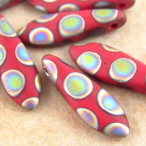 May include: Red glass beads with iridescent circles. The beads are shaped like a teardrop and have a hole at the top for stringing.