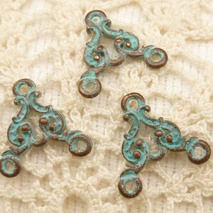May include: Three antique-style metal corner connectors with a turquoise patina and intricate scrollwork design. The connectors have two holes on each side for attaching to fabric or other materials.