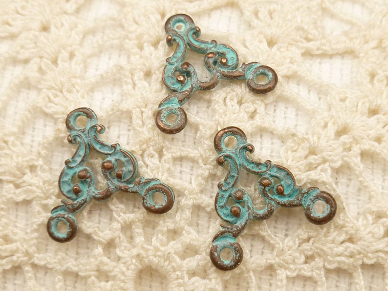 May include: Three antique-style metal corner connectors with a turquoise patina and intricate scrollwork design. The connectors have two holes on each side for attaching to fabric or other materials.