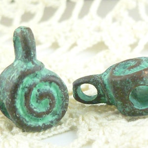 May include: Two green metal beads with a spiral design. One bead has a loop at the top and the other has a loop on the side.