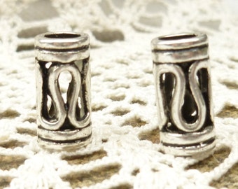 May include: Two silver metal hair beads with an intricate design. The beads are cylindrical and have a decorative pattern of interlocking loops.