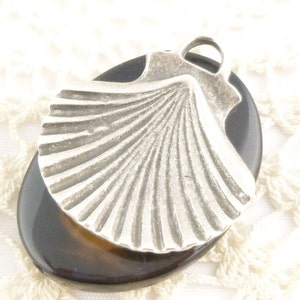 May include: A silver seashell pendant charm with a detailed design, set on a dark brown oval agate stone.