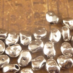 May include: A close-up of a pile of silver-colored metal beads. The beads are irregularly shaped and have a slightly rough texture. They are perfect for jewelry making or other craft projects.
