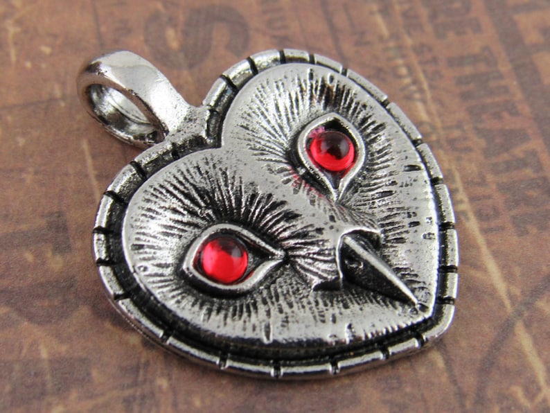 Peut inclure: Pendentif en forme de c&oelig;ur en argent avec un motif de hibou et des yeux en pierres pr&eacute;cieuses rouges.