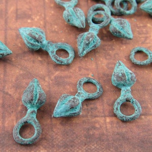 May include: A collection of teal-coloured metal charms with a pointed tip and a small loop. The charms are designed with a textured surface and are perfect for adding a unique touch to jewellery or crafts.