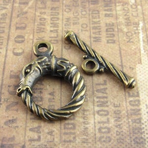 Può includere: Chiusura a toggle in ottone antico con un anello decorato con un'intricata testa di cavallo. La chiusura include una barra ritorta e un anello per una chiusura sicura. Ideale per la creazione di gioielli.
