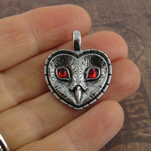 Peut inclure: Pendentif en forme de c&oelig;ur en argent avec un motif de hibou et des yeux en pierres pr&eacute;cieuses rouges.