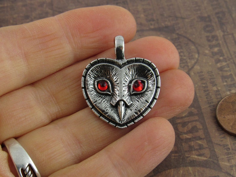 Peut inclure: Pendentif en forme de c&oelig;ur en argent avec un motif de hibou et des yeux en pierres pr&eacute;cieuses rouges.