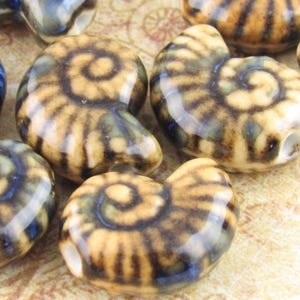 May include: A collection of ceramic beads in the shape of ammonite fossils. The beads feature a spiral design in shades of brown, tan, and blue. Each bead has a hole for stringing. These beads are suitable for jewelry making and other craft projects.