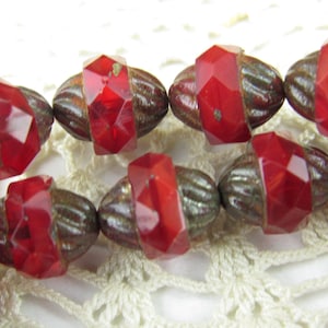 May include: A strand of red glass beads with a faceted design and silver-toned metal accents. The beads are oval-shaped and have a textured surface.