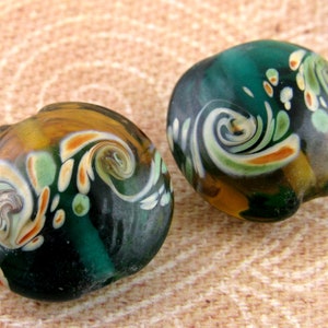 May include: Two round glass beads with a swirling pattern of green, white, and orange. The beads have a glossy finish.