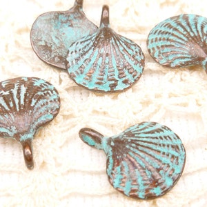 May include: Five turquoise and copper coloured metal shell charms with a loop for hanging. The charms are on a white lace background.