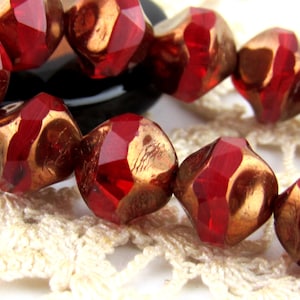 May include: Close-up of faceted red and gold beads. The beads have a geometric shape with multiple facets that reflect light. The gold color is visible on the inner surfaces of the beads, creating a contrast with the red exterior. The beads are strung together.