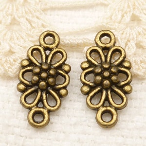 May include: Two antique gold-toned metal flower-shaped charms with a loop at the top. The charms have a detailed design with a central flower and a ring around it.