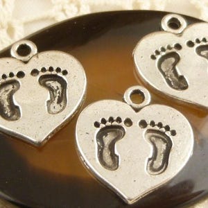 Puede incluir: Tres dijes de plata en forma de corazón con un diseño de huella de pie de bebé. Los dijes tienen un bucle en la parte superior para sujetarlos a un collar o pulsera.