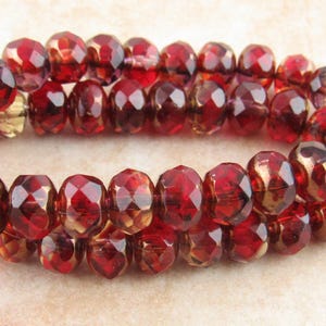 Könnte beinhalten: Nahaufnahme von Strängen facettierter, oval geformter Perlen in tiefem Rot und Gold. Die glänzenden Perlen sind aufgefädelt und erzeugen ein reichhaltiges, strukturiertes Aussehen. Ideal für die Schmuckherstellung.