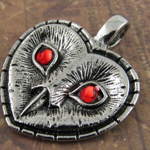 Peut inclure: Pendentif en forme de c&oelig;ur en argent avec un motif de visage de hibou. Le hibou a des yeux rouges et un bec d&eacute;taill&eacute;.