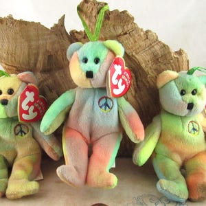 May include: Three tie-dye beanie baby bears with peace sign patches and Ty tags. The bears are green, yellow, orange, and blue.