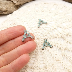 May include: Three turquoise blue metal triangle shaped connectors with decorative scrollwork. The connectors have three holes each for attaching jewelry or other crafts.