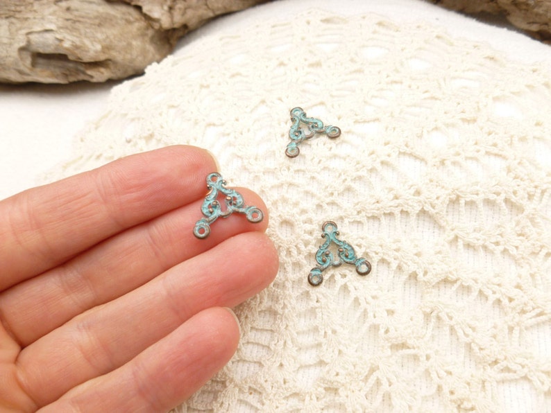 May include: Three turquoise blue metal triangle shaped connectors with decorative scrollwork. The connectors have three holes each for attaching jewelry or other crafts.