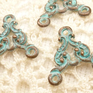May include: Three turquoise and copper-toned metal triangle-shaped embellishments with ornate scrollwork designs.
