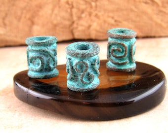 May include: Three cylindrical beads with a weathered turquoise patina and raised brown spiral patterns. Each bead features a central hole and a textured, aged finish, standing upright on a smooth, dark brown, polished stone surface.