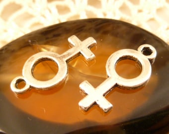 Puede incluir: Dos abalorios de metal plateado en forma de símbolo femenino. Los abalorios están sobre un fondo marrón.
