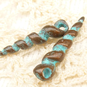 May include: Two bronze-colored, spiral-shaped pendants with turquoise accents. The pendants have a weathered, aged appearance, with a loop at the top for stringing. The design resembles a twisted horn or shell, suitable for jewelry making.