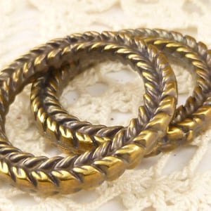 May include: Two gold-toned metal rings with a braided design. The rings are interlocked and have a shiny finish.