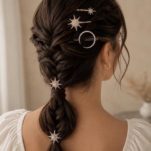 May include: A set of gold-toned hair accessories featuring three starburst designs encrusted with clear crystals and one circular clip with a crystal-lined rim. These decorative hair pins are arranged throughout a braided hairstyle.
