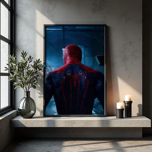 May include: A framed wall art print featuring a rear view of a superhero character in a textured red and blue suit with a prominent red spider emblem on the back. The character is depicted against a dark, moody blue background with subtle lighting.