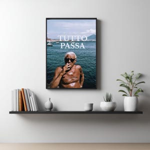 May include: A framed wall art print featuring a shirtless person with sunglasses smoking a cigarette against a backdrop of the sea and mountains. The text TUTTO PASSA is printed in white in the center of the image, and the same text is tattooed on the chest.