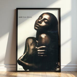Peut inclure: Une affiche encadrée présentant un portrait en noir et blanc à fort contraste de Sade. Le texte "sade love deluxe" figure dans le coin supérieur gauche et "released 26.10.92" est imprimé en bas à gauche. Le sujet a les yeux fermés.