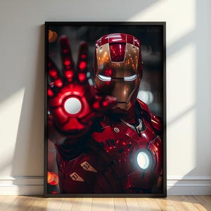 Op de afbeelding: Een ingelijste verticale poster met een metalen rood en goudkleurig harnas met een gloeiend wit cirkelvormig licht op de borst en handpalm. De helm heeft een glad, reflecterend oppervlak met smalle witte oogopeningen tegen een donkere achtergrond.