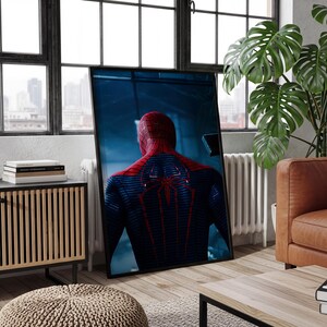 May include: A framed rectangular wall art print featuring a rear view of a superhero character in a textured blue and red suit with a prominent red spider emblem on the back, set against a dark, moody, and atmospheric blue background.
