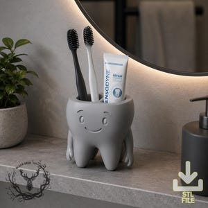 May include: A matte grey toothbrush holder shaped like a smiling tooth with two small arms. The holder contains one black toothbrush, one white toothbrush, and a tube of Sensodyne Repair & Protect toothpaste. The design features a simple face.
