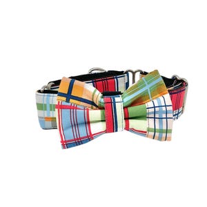 May include: A colorful dog collar with a plaid bow tie. The bow tie features a patchwork design with red, blue, green, and yellow plaid patterns. The collar has silver metal hardware and a black base.