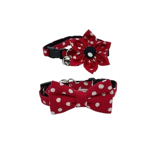 May include: Two red cat collars with white polka dots. One collar has a flower with a black center and a bell. The other collar has a matching bow tie. Both collars have black plastic buckles.