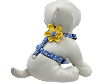 May include: A blue dog harness with a white floral pattern and a large yellow flower accent. The harness has adjustable straps and a metal D-ring for leash attachment. The dog harness is designed for small dogs.
