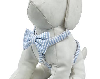 May include: A white dog harness with a blue and white striped pattern and a matching bow tie.