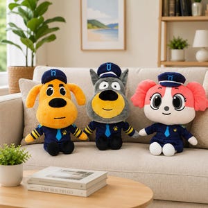 May include: Three plush toys dressed as pilots sitting on a sofa. The left toy is orange with floppy ears, the center toy is gray with pointed ears, and the right toy is white and pink with long ears. Each wears a navy blue uniform and cap.